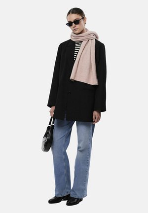 Blazer noir oversized, chemise rayée, jeans bleu clair, écharpe rose pâle, lunettes de soleil noires et petit sac à main noir ; look élégant et moderne.