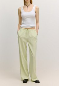 Witte cropped tanktop, lichtgroene wijde broek met elastische tailleband en trekkoord, gladde stof, zwarte schoenen, minimalistisch ontwerp.