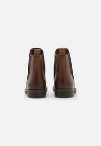 Brown leather ankle boots with black elastic panels, flat black soles, and orange stitching detail on the sides. Round toe design.