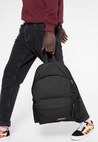 Mochila Eastpak negra hecha de material duradero, con un bolsillo frontal con cremallera, asa en la parte superior y correas acolchadas.