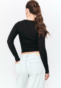Schwarzes langärmeliges, kurzes Oberteil, enganliegendes Design, glatte Textur. Kombiniert mit hellblauen High-Waist-Jeans mit Gesäßtaschen und einem Etikett.