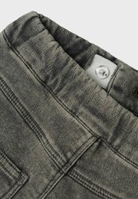 Tissu en denim gris avec une finition douce et texturée. Dispose d'une taille élastique, de poches cousues et d'une fermeture à bouton métallique.