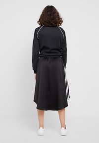 Svart sweatshirt med vit söm, kombinerad med en lång svart kjol med vita sidosträck. Bärs med vita sneakers.