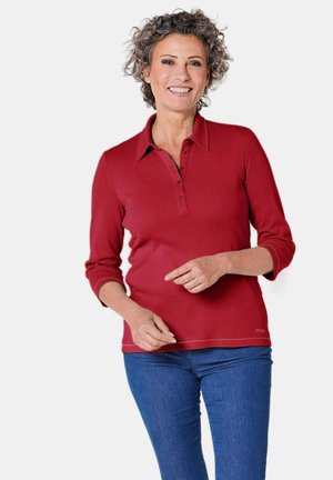 Polo shirt rosso a maniche lunghe con pattina a tre bottoni, texture a coste e dettagli di cucitura laterale, abbinato a jeans di denim blu.