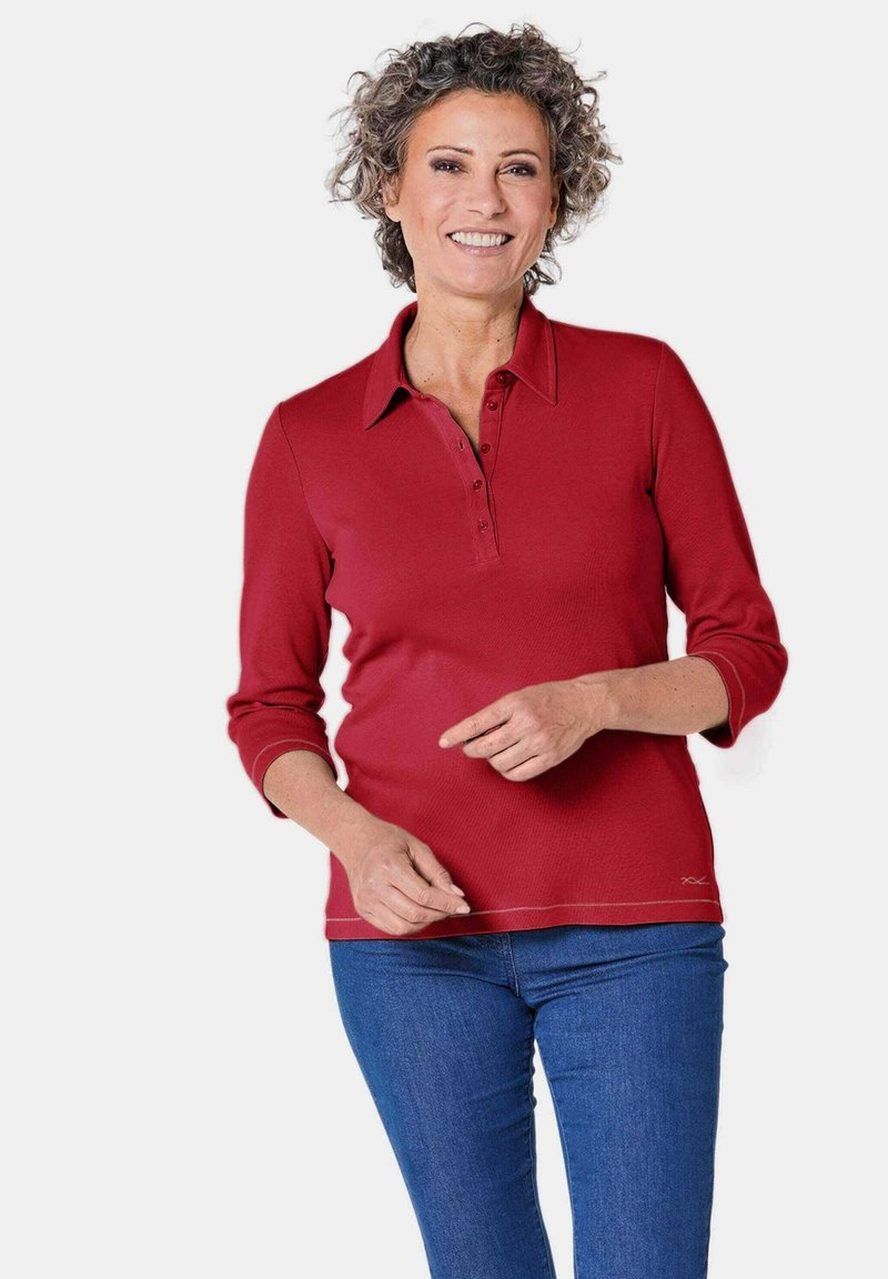 Rode polo shirt met lange mouwen, voorzien van een drie-knoopsluiting, ribbelstructuur en zijstiksels, gecombineerd met blauwe denim jeans.