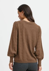 Brauner strukturierter Pullover mit einem Rautenmuster, der gepolsterte Ärmel und einen gerippten Saum aufweist. Der Stoff wirkt weich und leicht.