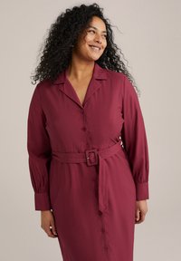Rochie căptușită de culoare vișinie, cu mâneci lungi, talie încinsă și material moale. Dispune de un guler clasic și o siluetă dreaptă.