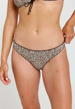 Kobieta w spodniej części bikini w panterkę, ręka na biodrze, jasny odcień skóry, neutralne tło.
