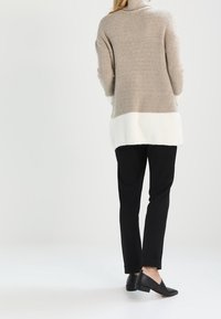 Sweter golf z dzianiny o ryflowanej fakturze, z beżowymi i białymi blokami kolorów. W komplecie z czarnymi spodniami i płaskimi butami.