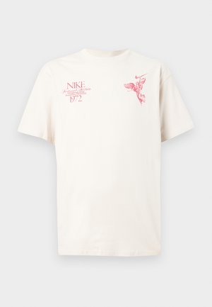 Krémové tričko s krátkým rukávem vyrobené z bavlny, zdobené červenými grafickými vzory a textem, včetně loga Nike a "1972" na přední straně.