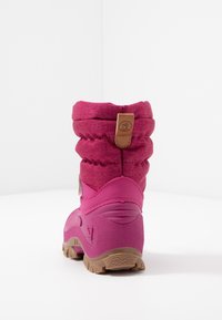 Bota de invierno rosa con parte superior de tela acolchada, suela de goma texturizada y asa marrón en un fondo blanco liso.