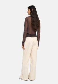 Brązowa, przezroczysta bluzka z długim rękawem, zestawiona z jasnobeżowymi, wysokim stanem, szerokimi spodniami o wykończeniu rozciętym na dole i gładkiej fakturze.