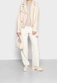 Kremowa skórzana kurtka motocyklowa, sweter z dzianiny, białe spodnie z szerokimi nogawkami i pleciona torebka. Grube, platformowe buty dopełniają zestaw.