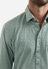 Groene blouse met een geometrisch patroon van ovale vormen, met een button-down kraag en zichtbare knopen. Katoenen stof met een gladde textuur.