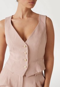 Rosa taillierter Weste mit tiefem V-Ausschnitt, vier goldenen Knöpfen und seitlichen Taschen. Hergestellt aus glattem Stoff mit figurnaher Passform.