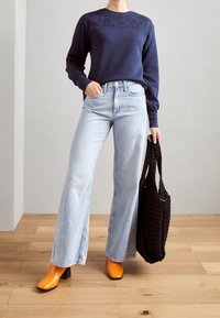 Felpa navy con ricami floreali, jeans a gamba larga blu chiaro, stivali arancioni con tacco e una borsa tote nera strutturata.