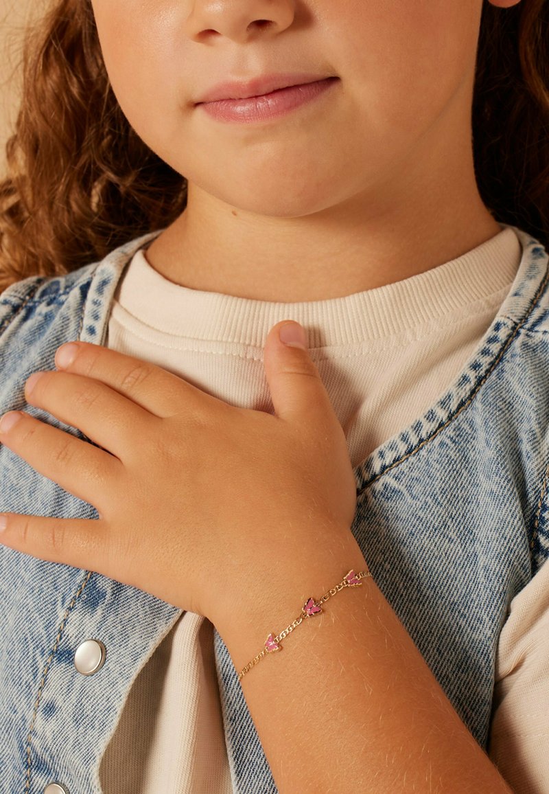 Goldkette mit Armbändern in Form von rosa Schmetterlingen, die am Handgelenk eines Kindes getragen wird, vor einem Hintergrund aus einer hellfarbigen Jeansjacke.