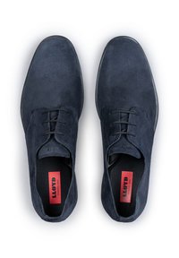Chaussures en daim bleu marine avec une texture lisse, un bout arrondi et un laçage. Présente des œillets noirs et un branding rouge sur les semelles intérieures.
