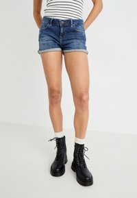 Denim shorts in medium blue with rolled hems, paired with black lace-up boots and white crew socks showcasing a textured pattern.