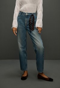 Svetlomodré džínsy s rovnými nohavicami a vysokým pásom, ku ktorým je voľne previazaný čierny šál s bodkami na páse; doplnené čiernymi balerínami.