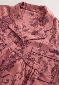 Rosa Pyjama-Set mit dunklen Blumen- und Rebenmustern, mit einem Knopfkragen und einer Brusttasche sowie elastischem Bund an der Hose.