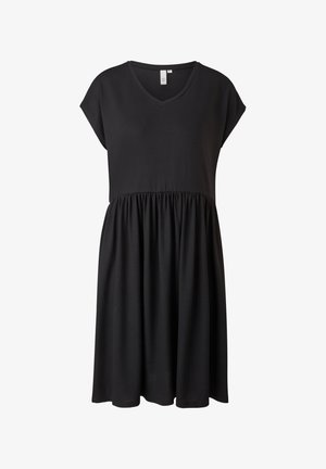 Donna che indossa un vestito nero largo a maniche corte con scollo a V e vita arricciata, abbinato a sandali bianchi piattaforma con cinturini.