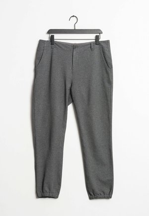 Pantalon de survêtement gris fuselé avec poignets élastiques, poches latérales et fermeture à bouton suspendu sur un cintre noir sur un fond blanc.