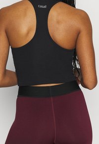 Černý žebrovaný crop top s designem racerback, kombinovaný s burgundskými legínami s vysokým pasem a černým pasem.