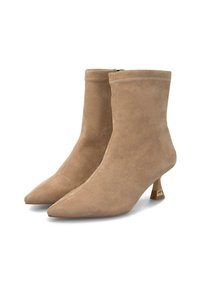 Un par de botines de ante beige con puntera afilada y bajos tacones de estilete con detalles dorados, sobre un fondo blanco.