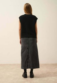 Svart stickad ärmlös topp i kombination med en grå denim maxikjol. Mörka byxor har en mittsöm och bakfickor, bärs med svarta skor.