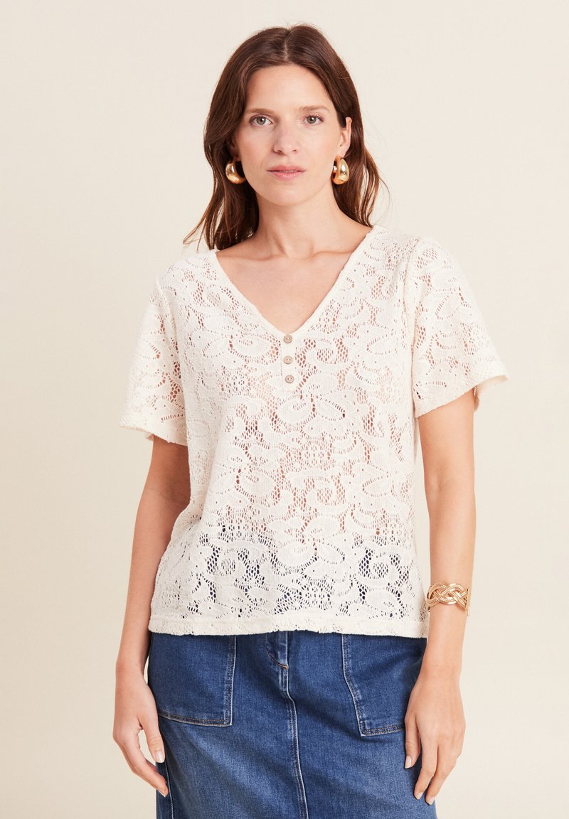 Top in pizzo color crema con maniche corte, scollatura a V profonda e tre bottoni sul davanti; presenta un motivo floreale e una finitura testurizzata.