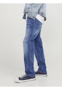 Jeans de denim azul con un corte relajado, que presentan un ligero desgaste, diseño de cinco bolsillos y acentos de costura en contraste, combinados con zapatillas oscuras.