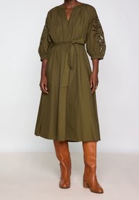 Olivově zelené midi šaty s zapínáním na knoflíky, vázáním v pase a vypouklými rukávy se střižením. V kombinaci s karamelovými kozačkami po kolena.