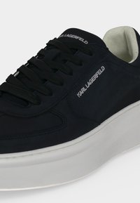 Μαύρο sneaker Karl Lagerfeld με μαύρα κορδόνια, λευκή παχιά σόλα και λογότυπο της μάρκας στο πλάι και στη γλώσσα, εμφανίζεται σε λευκό φόντο.