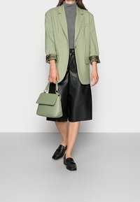 Jasnozielony, oversize'owy żakiet z satynowymi detalami przy mankietach, szary golf, czarne kuloty z materiału sztucznej skóry oraz czarne loafersy. Zielona torebka z uchwytem.