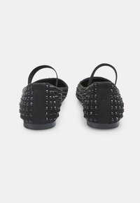 Bailarinas negras con un acabado de ante texturizado, adornadas con brillantes tachuelas negras en los lados. Cuentan con correas en el talón elásticas para un ajuste seguro.