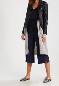 Svart läderjacka över en grå cardigan, i kombination med en svart plisserad topp och marinblå culottes, kompletterad med metalliska slip-on skor.