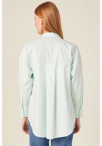 Camicia di cotone verde chiaro con strisce verticali bianche, maniche lunghe, colletto a punta e design con pieghe sul retro.