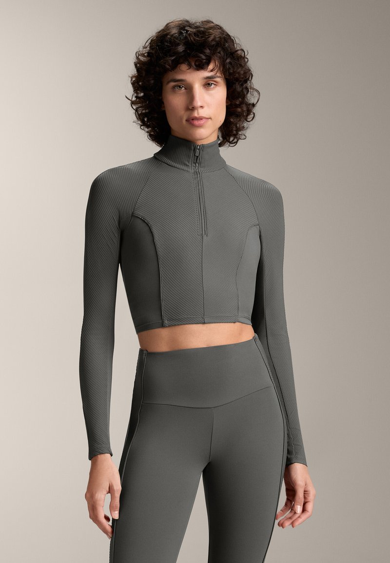 Šedý, ribbovaný crop top s dlhým rukávom, vysokým golierom a štvrť zipsom; doplnený o zodpovedajúce legíny s vysokým pásom pre koherentný vzhľad.