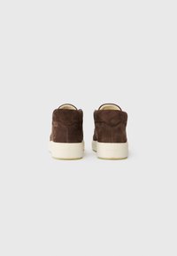Adidași bej din suede, cu glezna înaltă și talpă din cauciuc alb, având o textură netedă și un design minimalist, cu detalii de cusătură vizibile la spate.