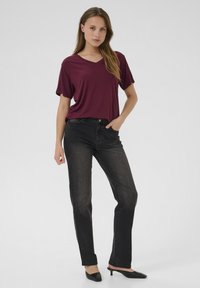 T-shirt V en bordeaux, coupe décontractée, associé à un jean en denim noir. Des mules à talons noires complètent le look décontracté. Textures de tissu lisse visibles.