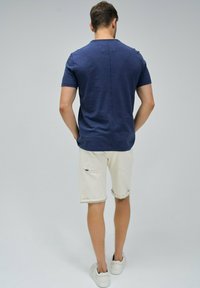 Ciemnoniebieska koszula z krótkim rękawem o prostym kroju, zestawiona z kremowymi, podwiniętymi szortami dżinsowymi i białymi trampkami. Minimalistyczny design.