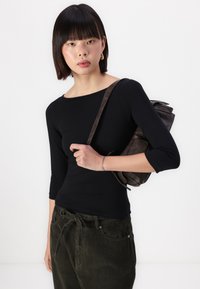 Zwarte lange mouwen top met een ronde hals, gecombineerd met groene corduroybroek. Een donkere leren tas hangt van de schouder.