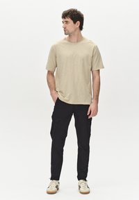 Beige short-sleeve t-shirt made of soft fabric, paired with black cargo pants featuring side pockets. Footwear includes beige sneakers.