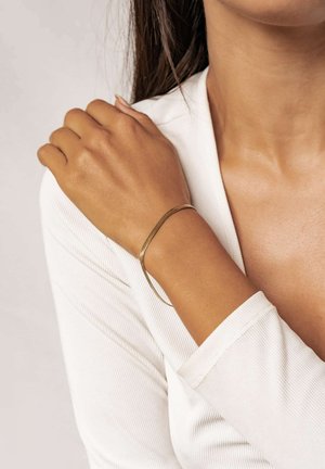 Goldenes Metallarmband an einem Handgelenk, mit einem schlanken, minimalistischen Design und einer glatten, polierten Oberfläche. Strukturierter Ärmel eines weißen Kleidungsstücks sichtbar.