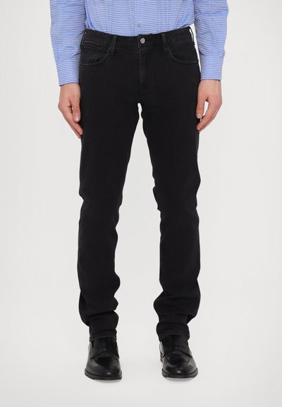 Jeans negre din denim cu o croială slim, cinci buzunare și detalii subtile de cusătură, asortate cu pantofi negri din piele.