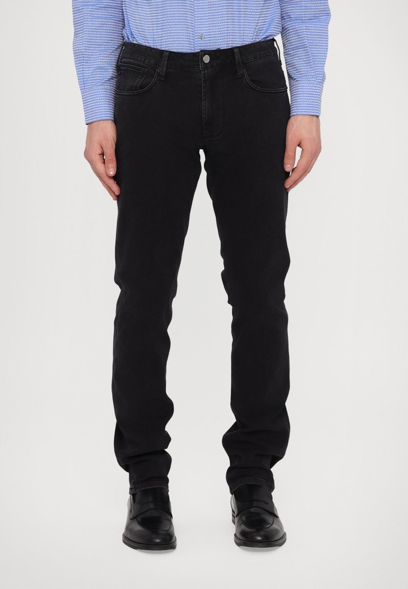Schwarze Jeans aus Denim mit einer schmalen Passform, fünf Taschen und dezenten Nähten, kombiniert mit schwarzen Lederschuhen.