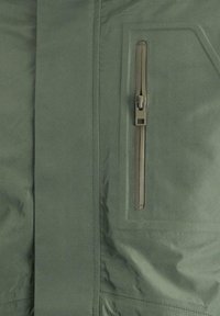 Tessuto della giacca verde oliva con una texture liscia, caratterizzato da una tasca con zip verticale sulla parte anteriore e dettagli cuciti.
