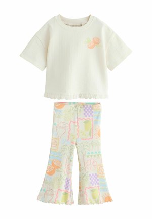 Crèmekleurige top met korte mouwen met ruches aan de zoom en oranje fruitprint gecombineerd met pastel kleurige uitlopende broeken met kleurrijke fruit- en bloemenpatronen.