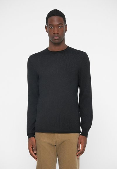 Sort langærmet sweater med et struktureret mønster og rund halsudskæring, parret med beige corduroy bukser. Minimalistisk design, tætsiddende silhuet.